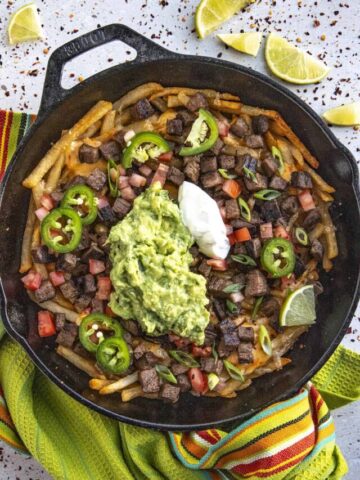 Carne Asada Fries topped with guacamole, crema, sliced jalapenos, tomato, and green onion