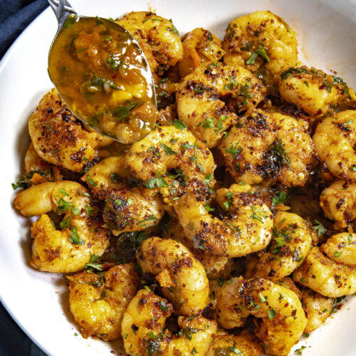 Spooning extra chimichurri over Chimichurri Shrimp in a bowl