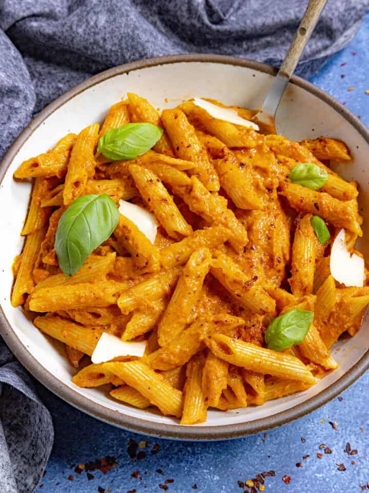 Roasted Red Pepper Pasta in a bowl, garnishd with fresh basil and shaved parmesan cheese