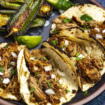 Crispy Mexican carnitas (pulled pork tacos) on a plate, served with chiles toreados