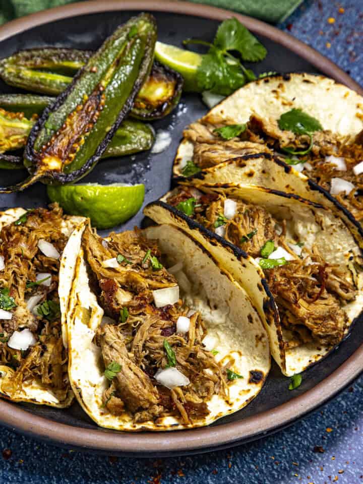 Crispy Mexican carnitas (pulled pork tacos) on a plate, served with chiles toreados
