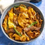 A bowl of wide, flat noodles mixed with slices of beef, green onions, and bean sprouts offers a delicious beef chow fun experience. The dish is coated in a rich, dark sauce.