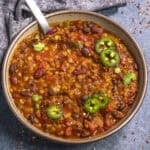 A close-up of a bowl filled with hearty lentil chili. The chili consists of kidney beans, black beans, tomatoes, and lentils, mixed in a rich, red sauce.