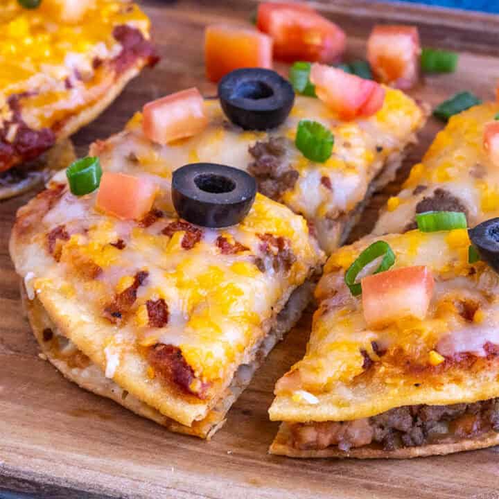 Close-up of a Taco Bell-style Mexican Pizza sliced into 4 pieces, garnished with chopped tomato, black olives, and green onion