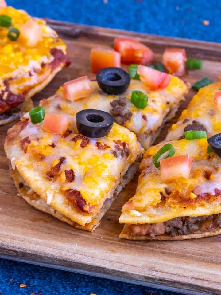 Close-up of a Taco Bell-style Mexican Pizza sliced into 4 pieces, garnished with chopped tomato, black olives, and green onion