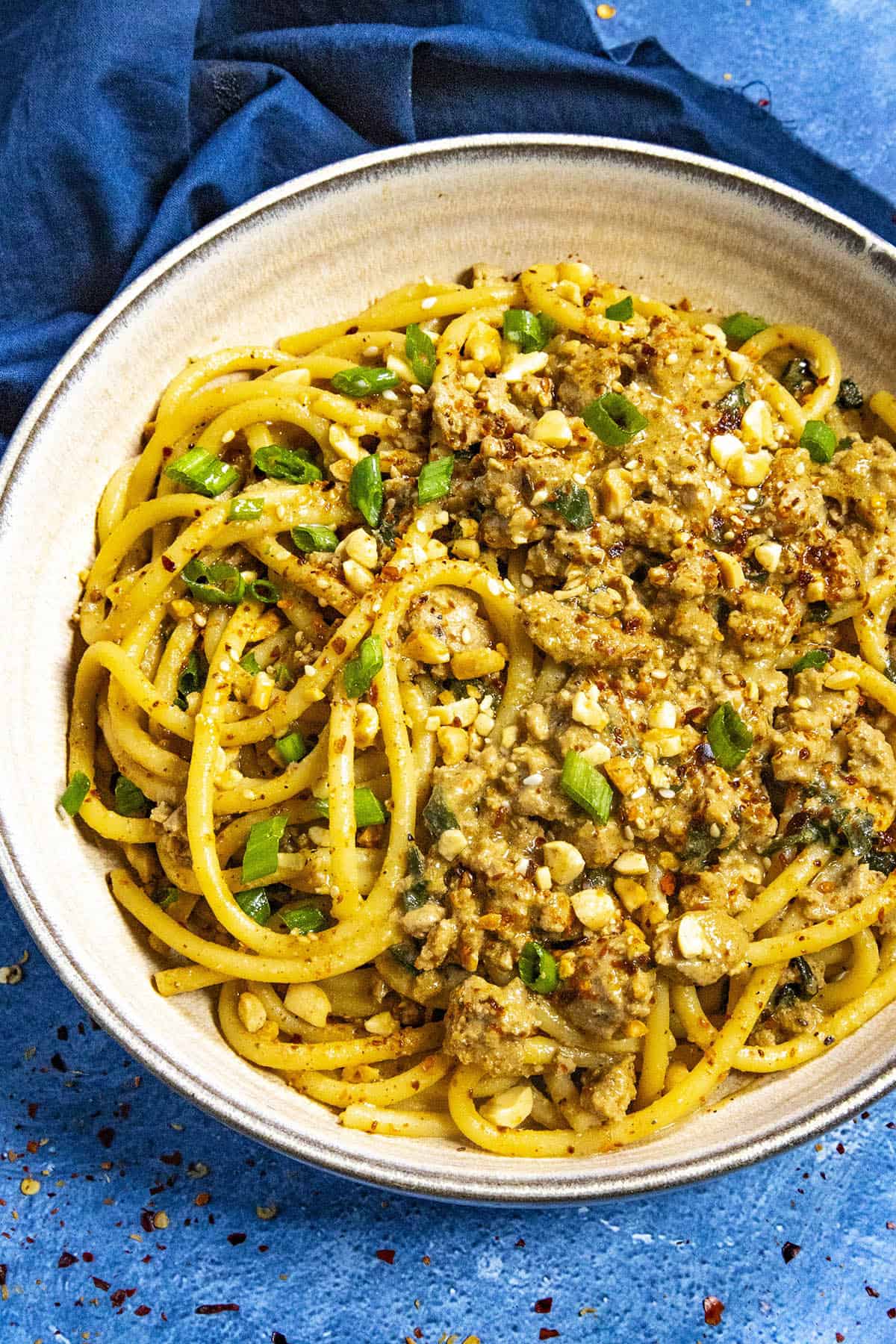 Dan Dan Noodles served in a bowl, garnished with roasted peanuts, sesame seeds, chili flakes, and sliced green onion