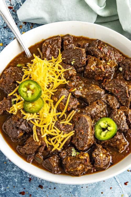 A meaty bowl of Texas Chili served with shredded cheese and sliced chilies on top