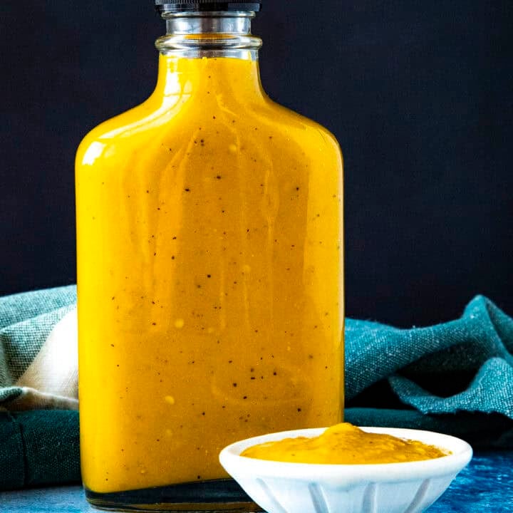 A bottle of spicy, vibrant yellow Bajan Hot Sauce on a table with a bowl of hot sauce beside it