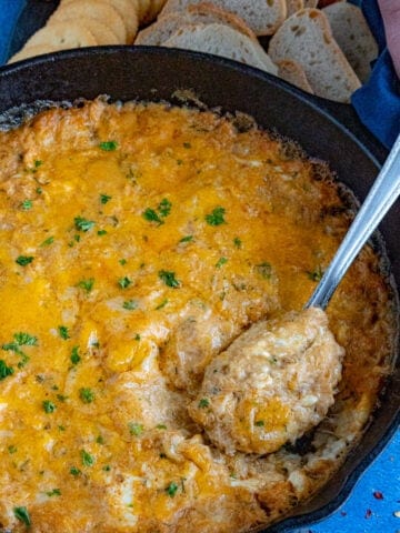 Taking a scoop from the pan of hot crab dip with a spoon to serve