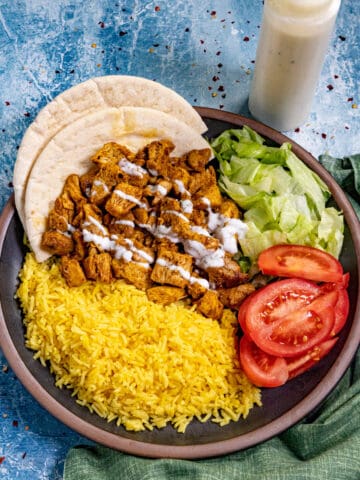 (Halal Cart Style Chicken on a serving plate with yellow rice, simple salad, drizzled with Halal white sauce