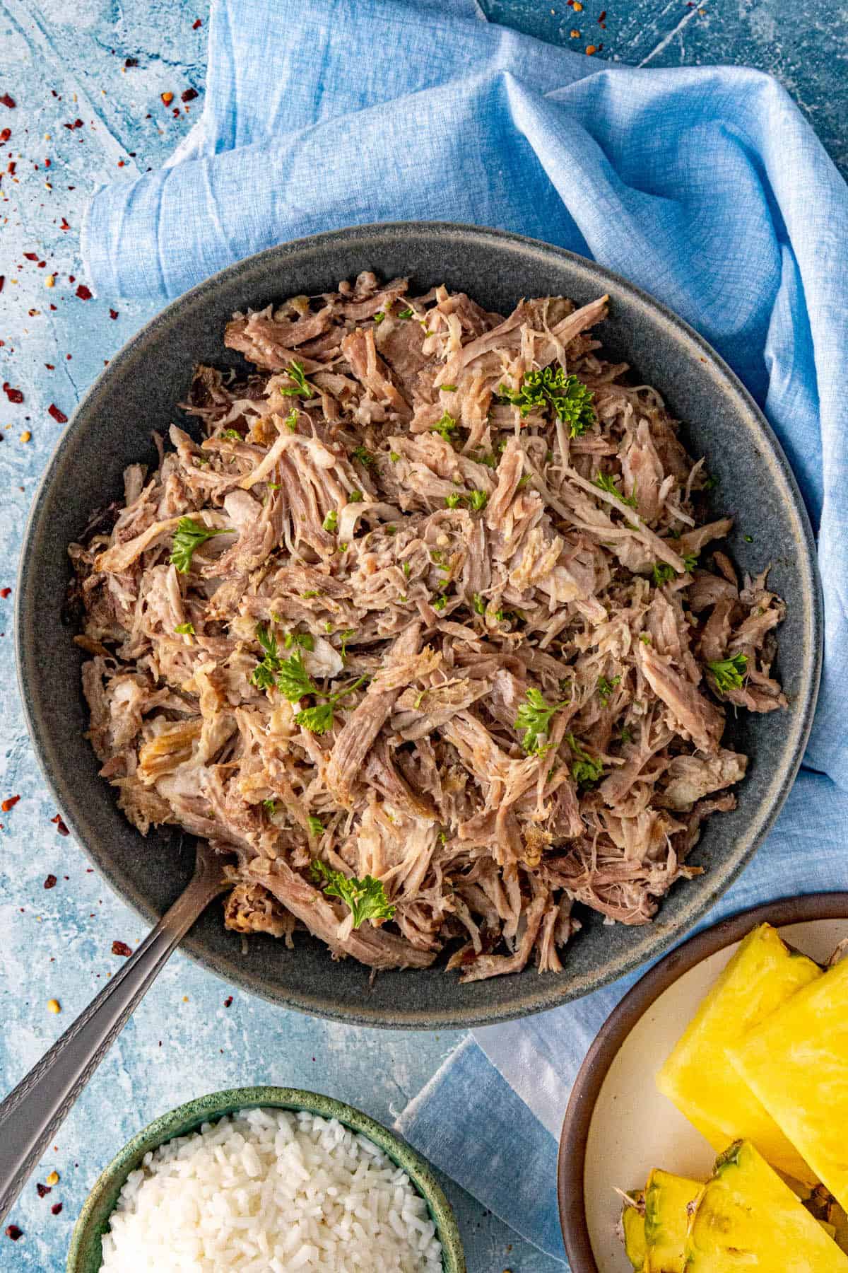 A bowl of smoky Kalua Pork served with white rice and sliced pineapple on the site