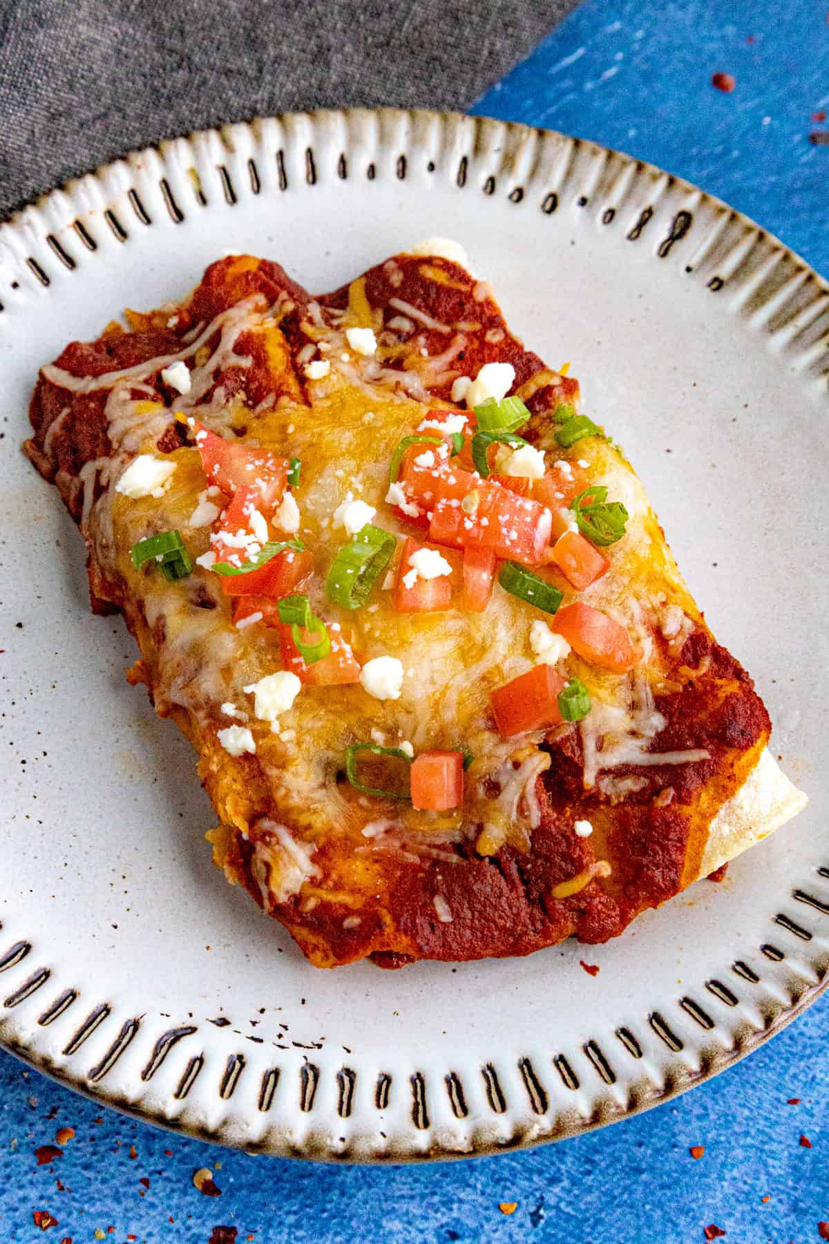 Two cheese enchiladas served on a plate, garnished with chopped tomato and green onion
