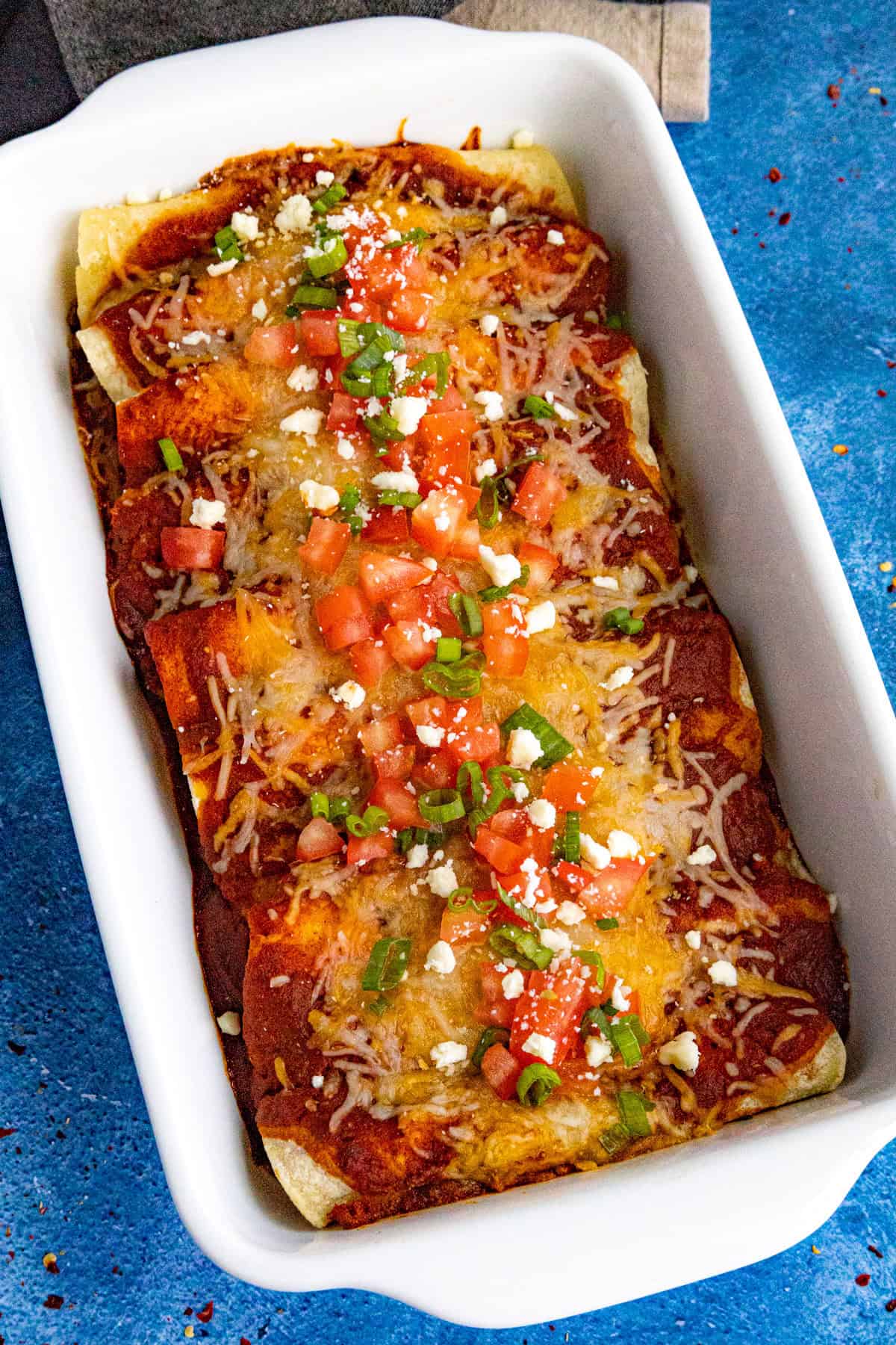 A baking dish of Cheese Enchiladas just out of the oven, garnished with chopped tomato and green onion