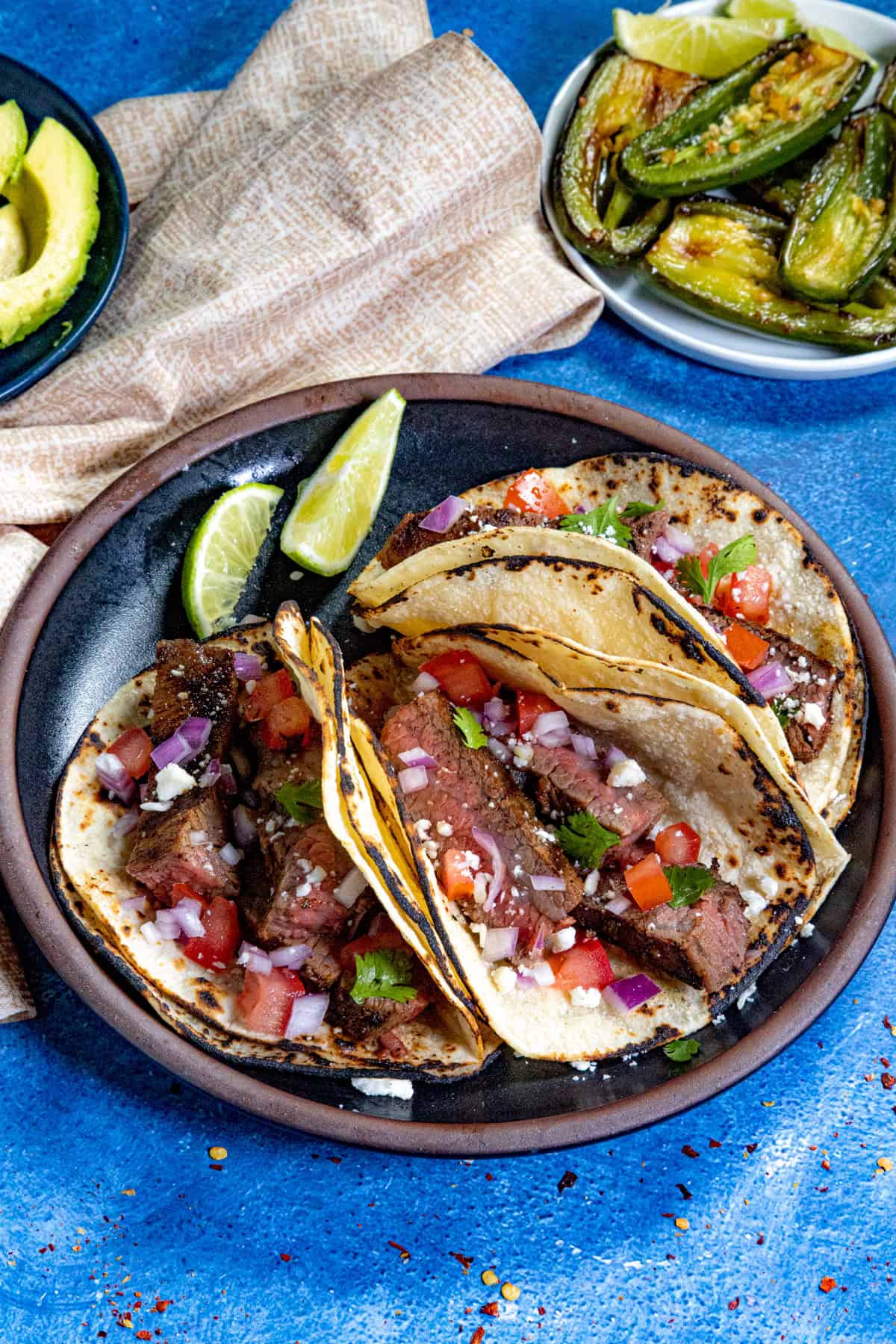 Three Steak Tacos served with onion, tomato, cilantro, and lime wedges