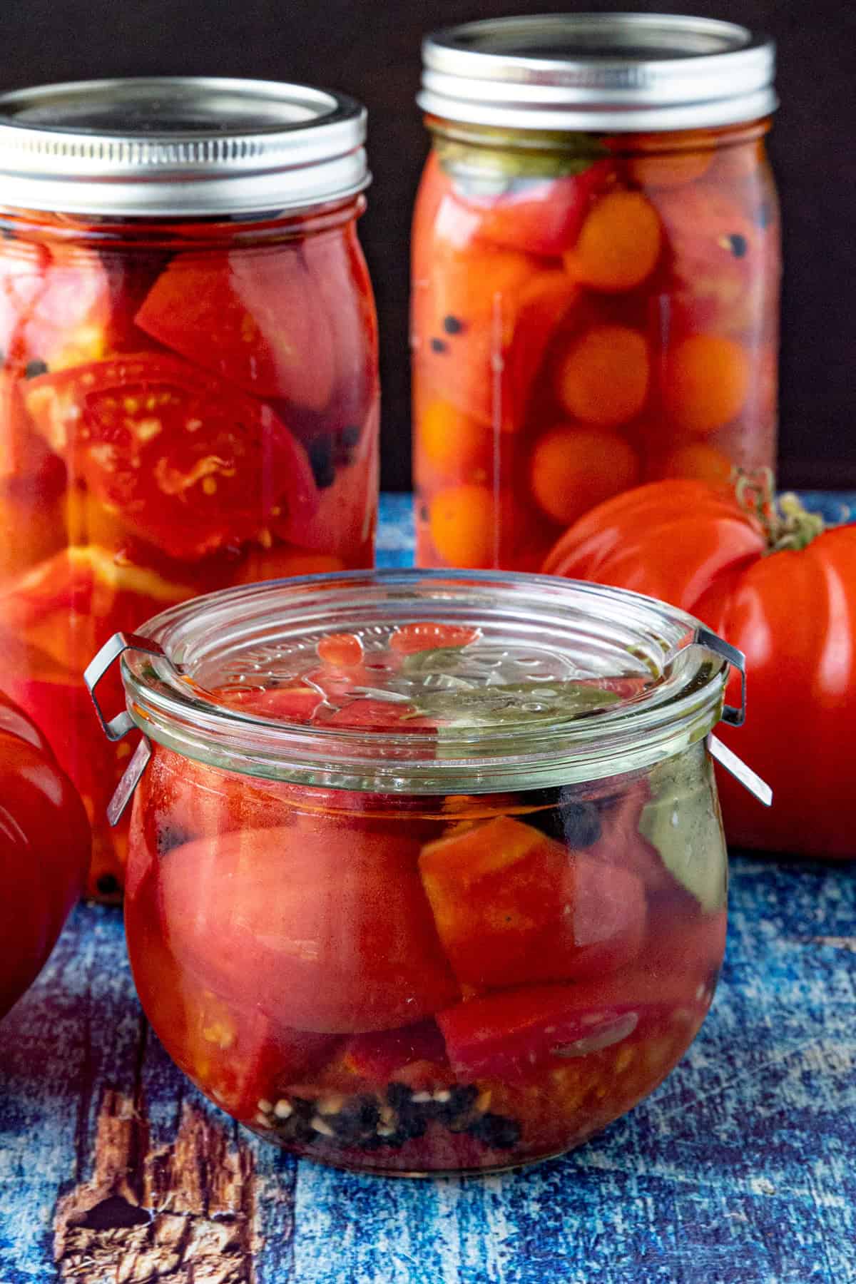 3 jars of Pickled Tomatoes on a table with beefsteak tomatoes