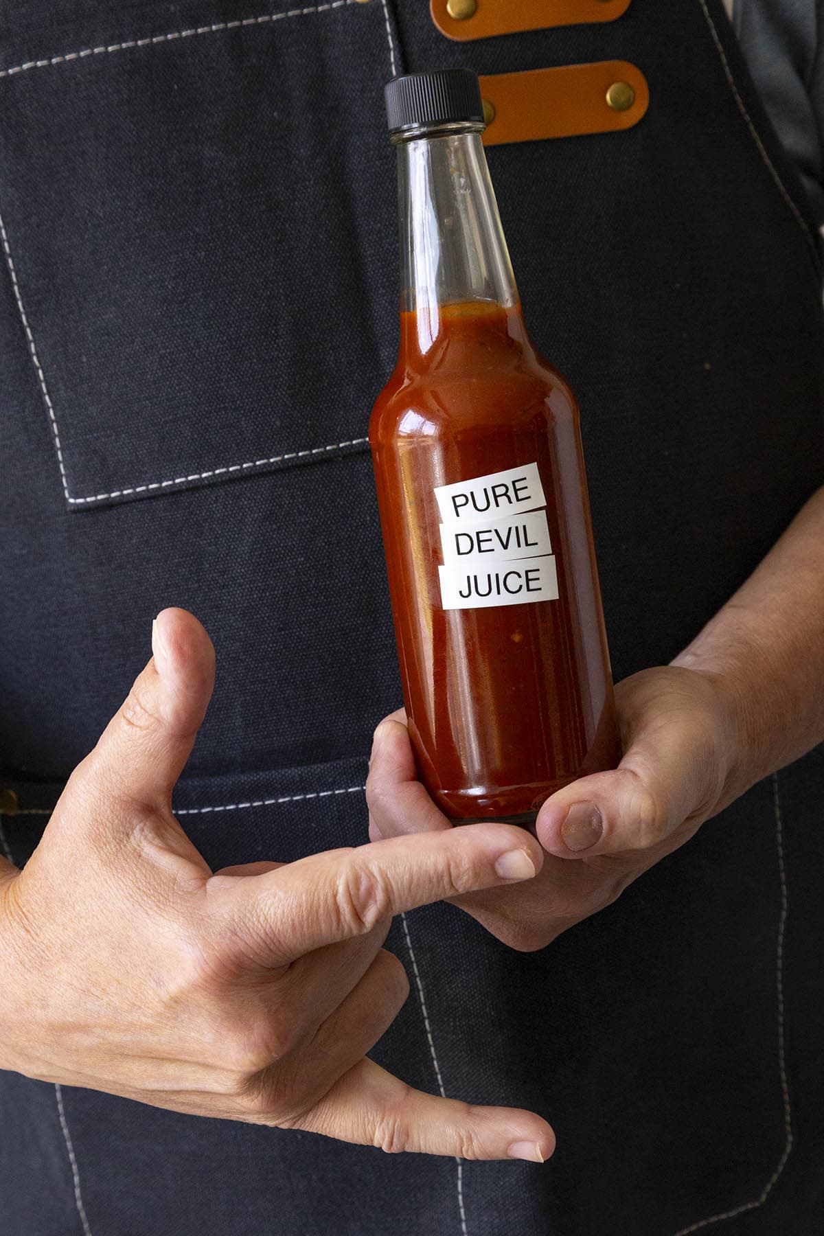 Mike holding a bottle of Pure Devil Juice hot sauce, and making devil's horns gesture with his hand