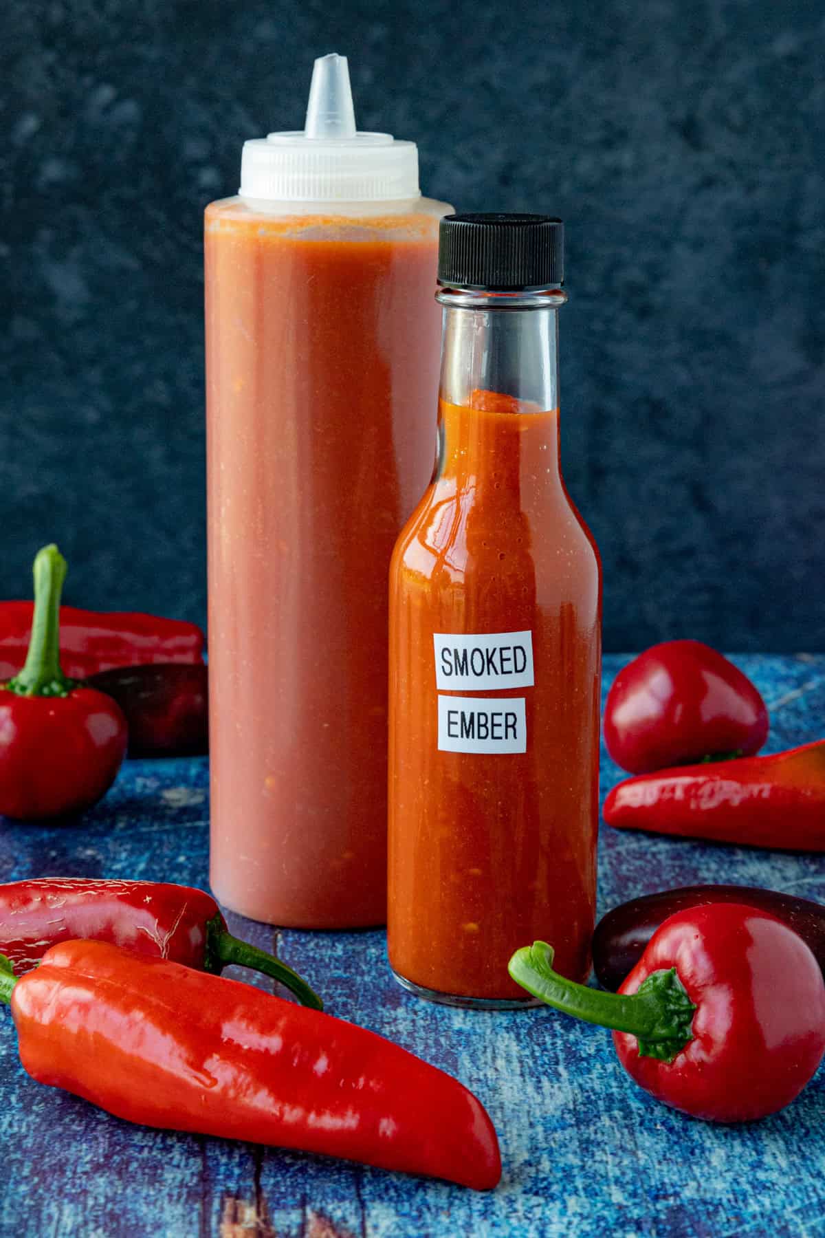 2 bottles of Smoked Chili Hot Sauce (Smoked Ember) on a table with extra chili peppers