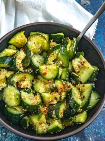 A bowl of Asian Cucumber Salad with a serving spoon, garnished with sesame seeds and chili flakes