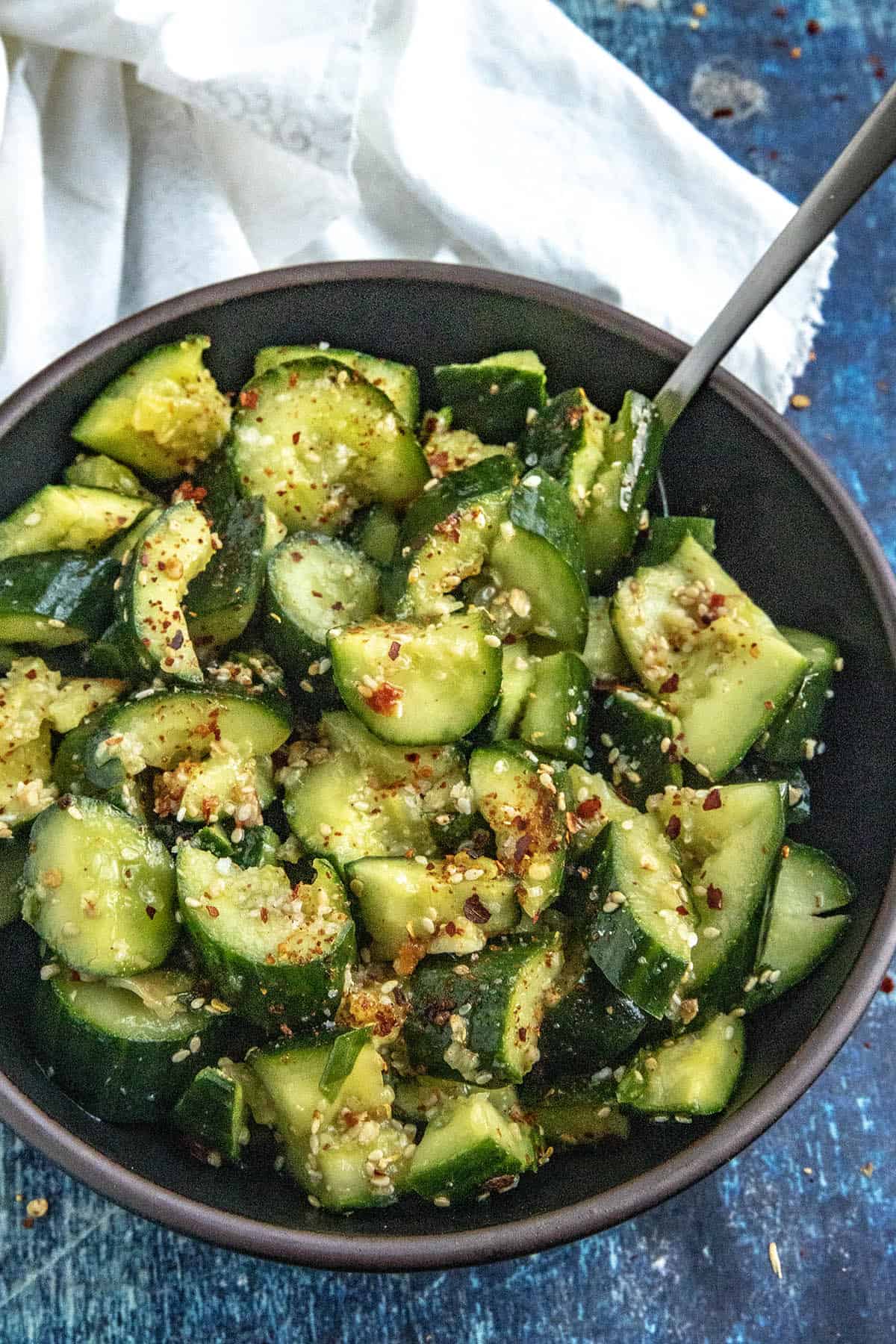 A bowl of Asian Cucumber Salad with a serving spoon, garnished with sesame seeds and chili flakes