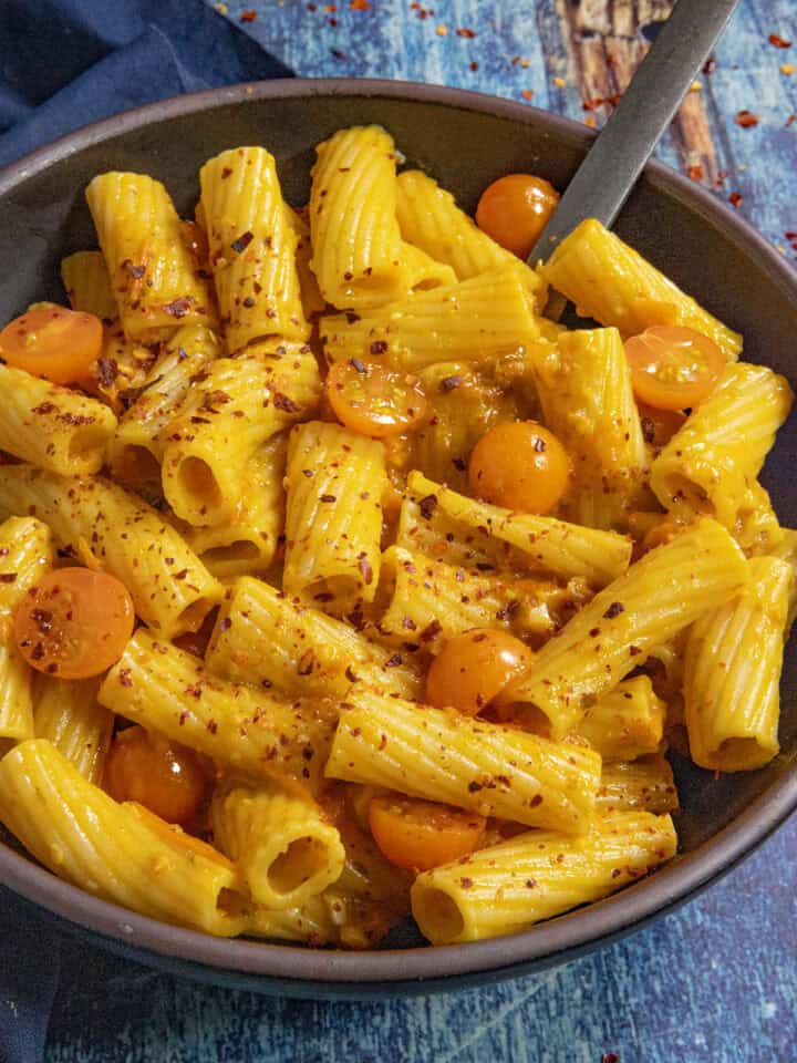 A small bowl filled with penne pasta, served with Tuscan-style Cherry Tomato Pasta Sauce and extra cherry tomatoes