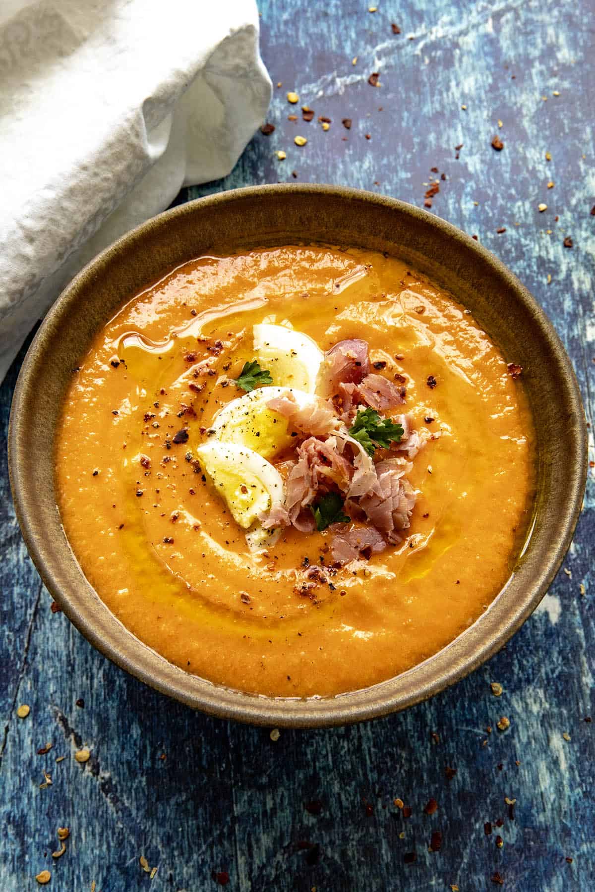 Creamy Salmorejo (Spanish Cold Tomato Soup) served in a small bowl, garnished with hard boiled egg, sliced ham, and olive oil