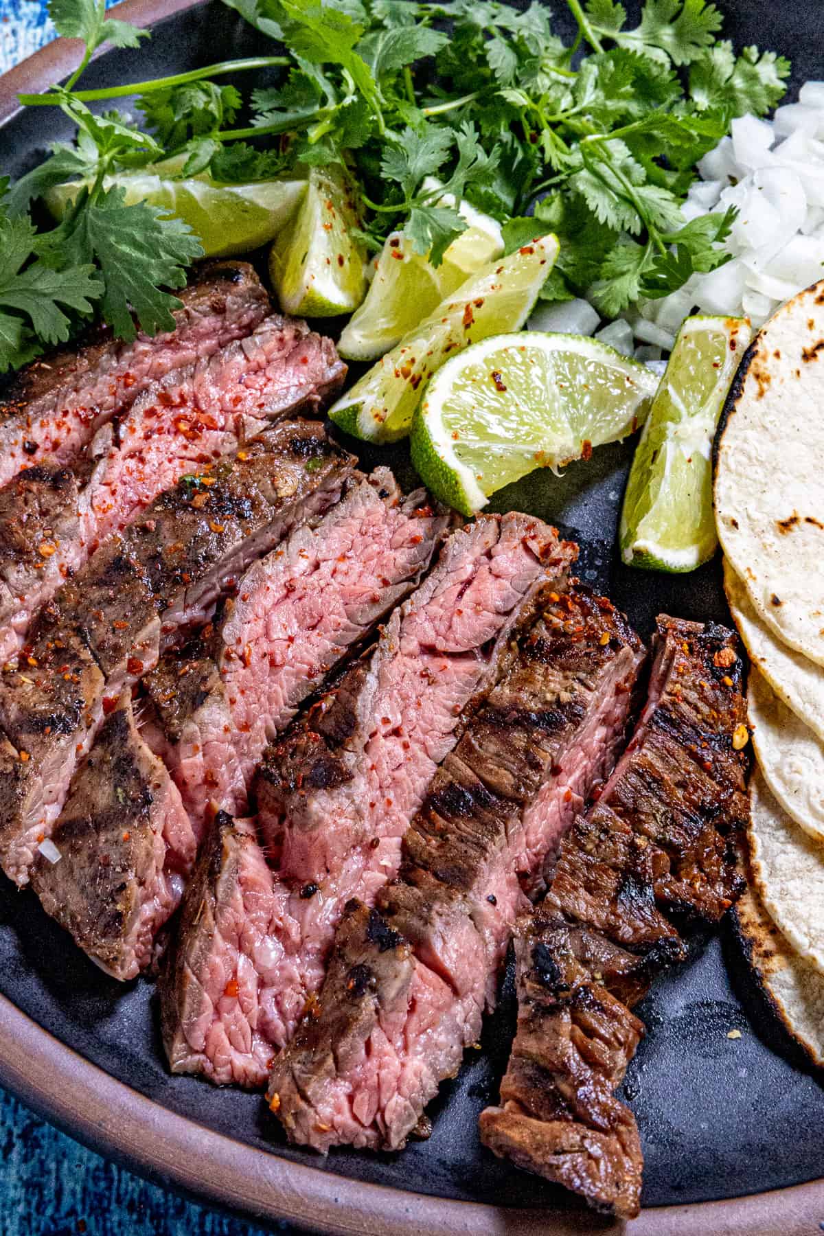 Close up of Mexican Skirt Steak (Arrachera) served on a plate with tortillas and toppings
