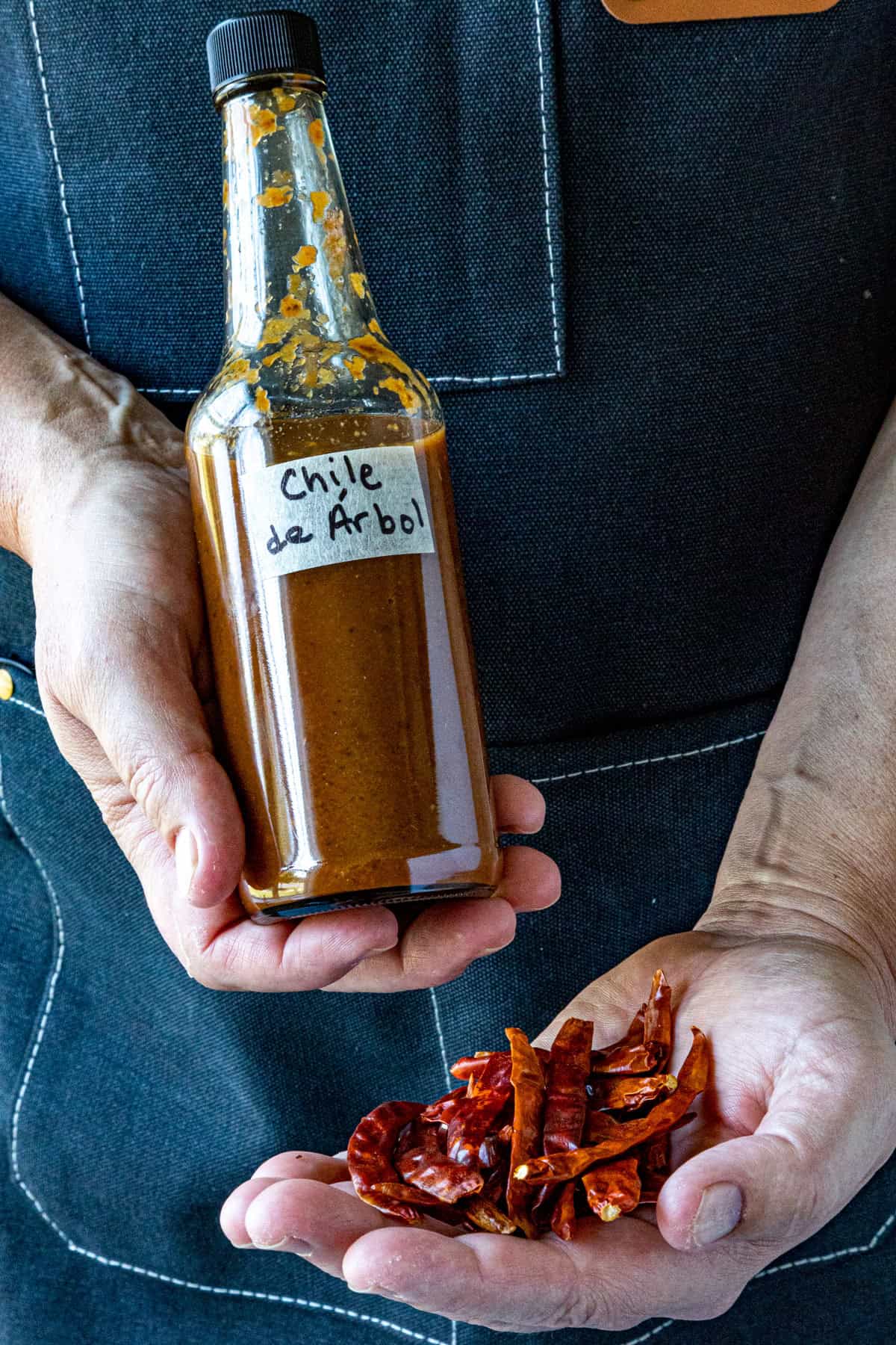 Mike holding a bottle of Chili de Árbol Hot Sauce and dried chiles de arbol