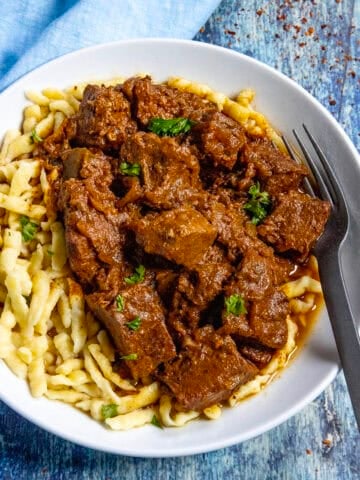 A large bowl of Hungarian Porkolt served over nokedli (noodles), with a fork