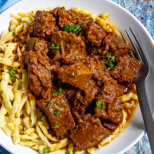 A large bowl of Hungarian Porkolt served over nokedli (noodles), with a fork