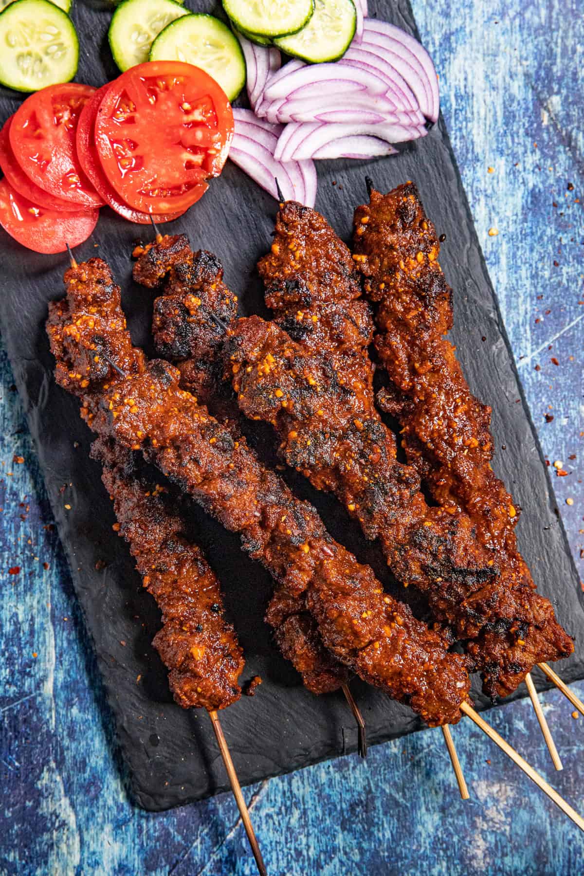 Spicy African Grilled Beef Skewers (Suya) served on a platter with sliced red onion, tomatoes, and cucumbers