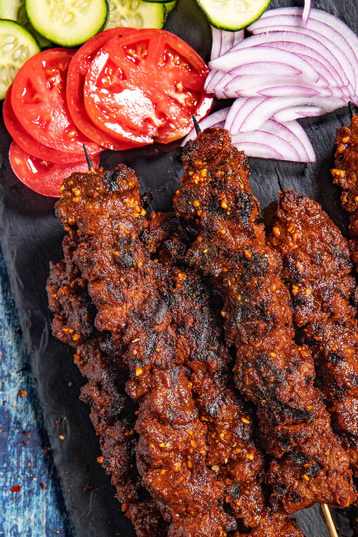 Spicy African Grilled Beef Skewers (Suya) served on a platter with sliced red onion, tomatoes, and cucumbers