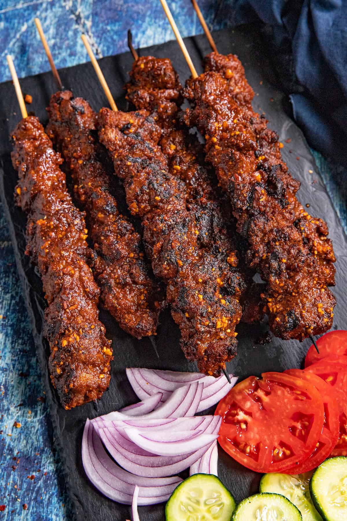 African Grilled Beef Skewers (Suya) served with sliced red onion, tomatoes, and cucumbers