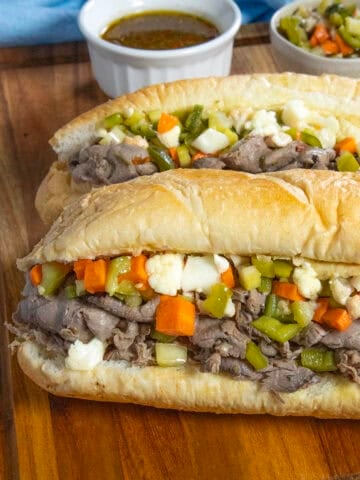 Two Chicago Italian Beef Sandwiches served with extra Chicago-style giardiniera in a bowl and beef jus on the side