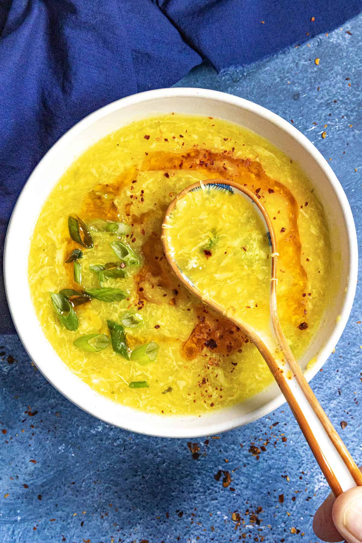 Chinese egg drop soup in a bowl with a spoon, topped with spicy chili oil