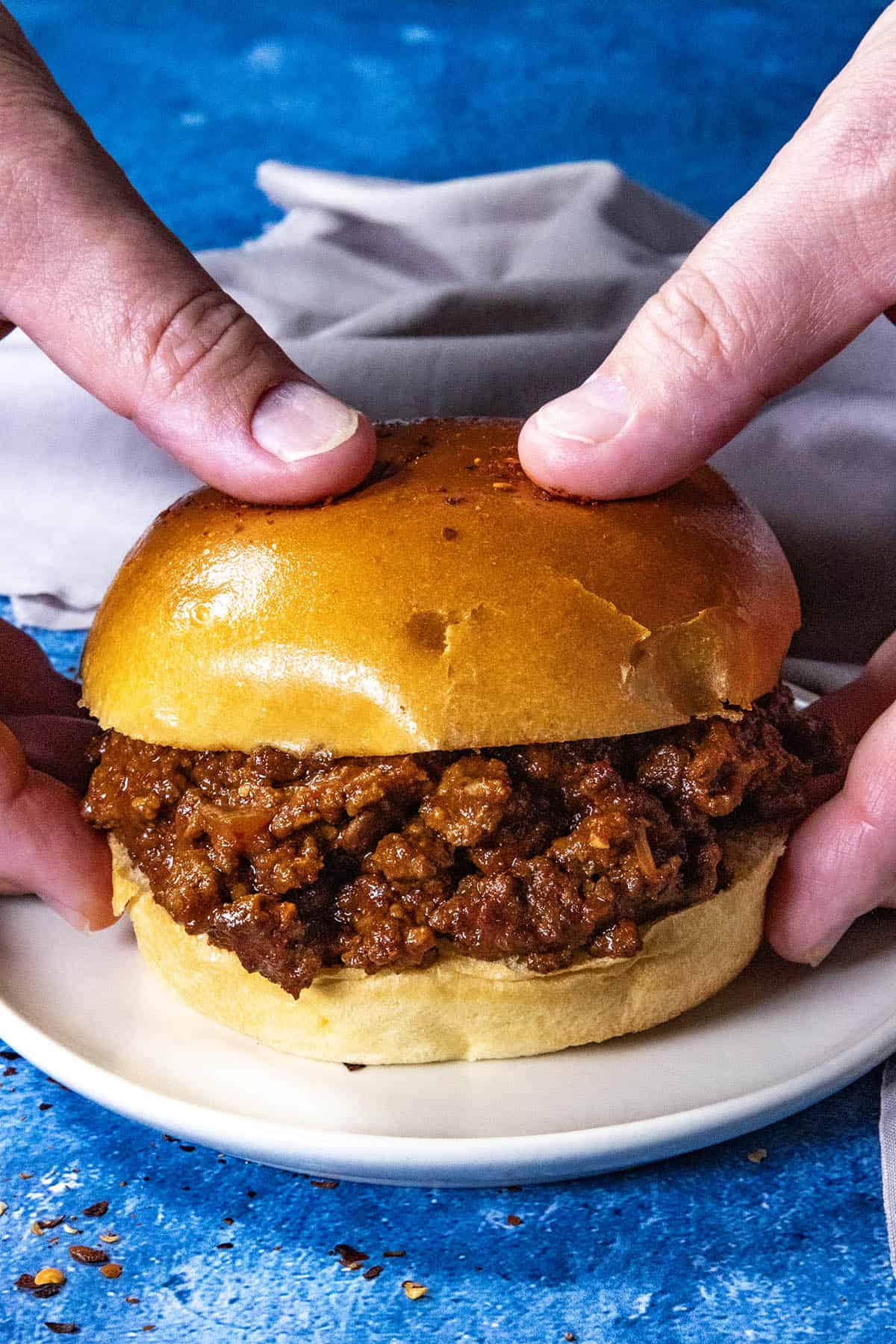 Mike grabbing a sticky-sweet, spicy, saucy Gochujang Sloppy Joes sandwich from the plate