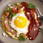 Huevos Rancheros on a plate - a warmed corned tortilla topped with creamy refried beans, a fried egg, ranchero sauce, and pico de gallo