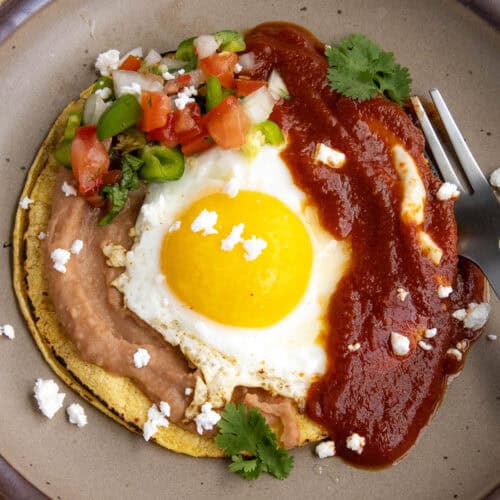 Huevos Rancheros on a plate - a warmed corned tortilla topped with creamy refried beans, a fried egg, ranchero sauce, and pico de gallo