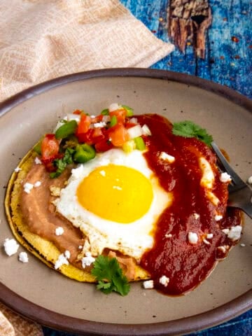 Mexican Huevos Rancheros on a plate, with a sunny-side-up egg served over tortillas with refried beans and ranchero sauce