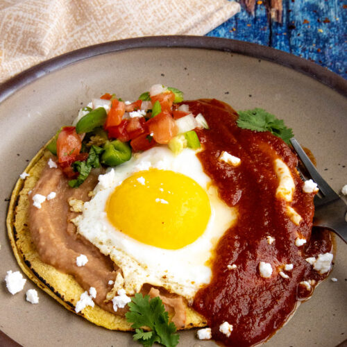 Mexican Huevos Rancheros on a plate, with a sunny-side-up egg served over tortillas with refried beans and ranchero sauce