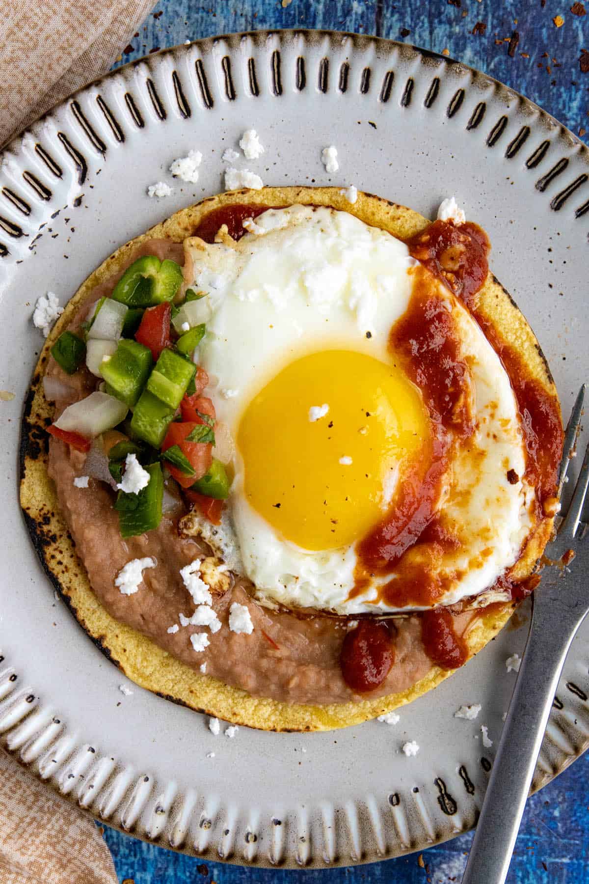 A sunny-side-up egg served over tortillas with refried beans and ranchero sauce and pico de gallo - Mexican Huevos Rancheros