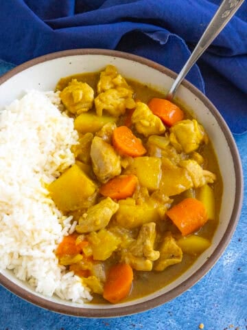 A bowl filled with hearty Japanese style curry with lots of potatoes and carrots, served with rice