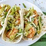 Fish tacos on a plate served with creamy jalapeno sauce, topped with crunchy slaw