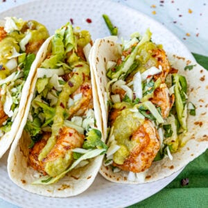 Fish tacos on a plate served with creamy jalapeno sauce, topped with crunchy slaw