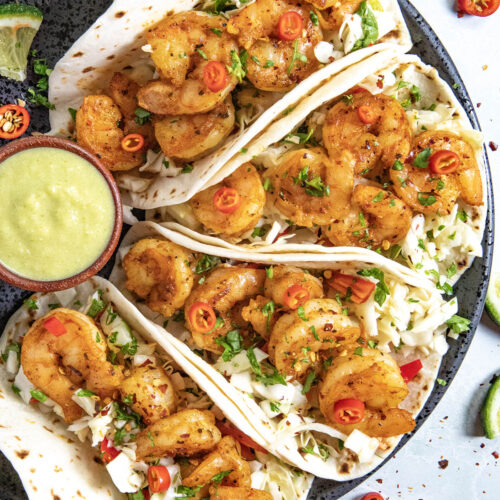 Four fish tacos on a plate served with creamy jalapeno sauce, topped with crunchy slaw