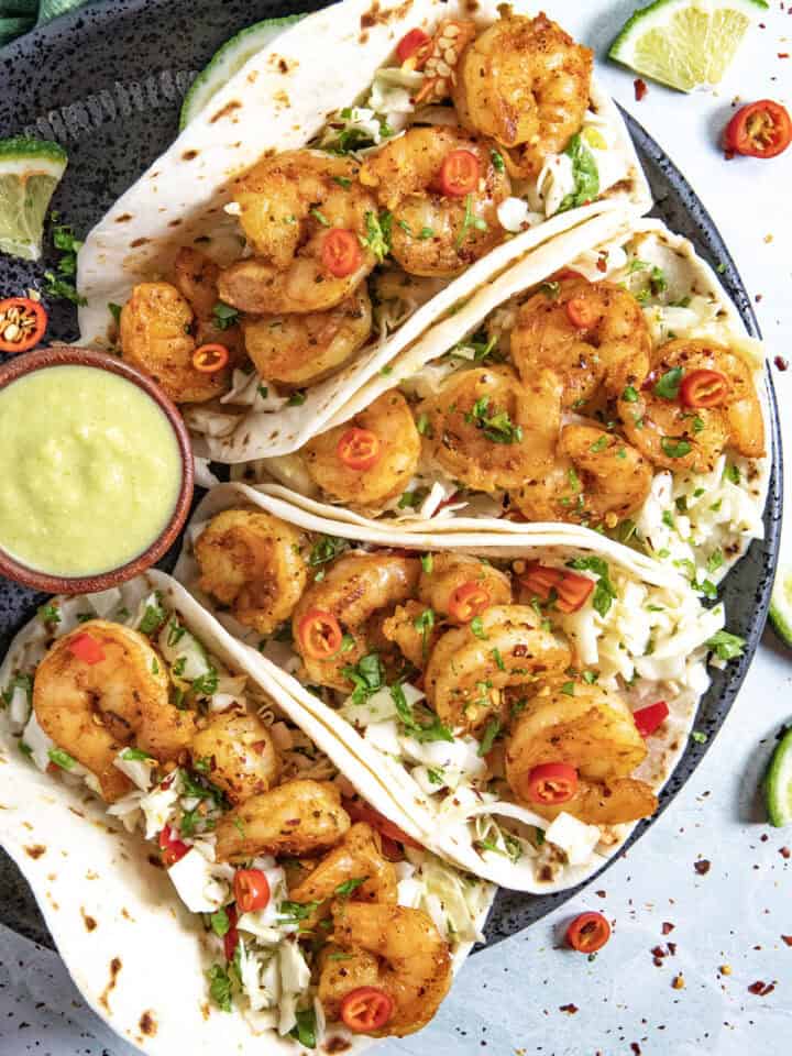 Four fish tacos on a plate served with creamy jalapeno sauce, topped with crunchy slaw