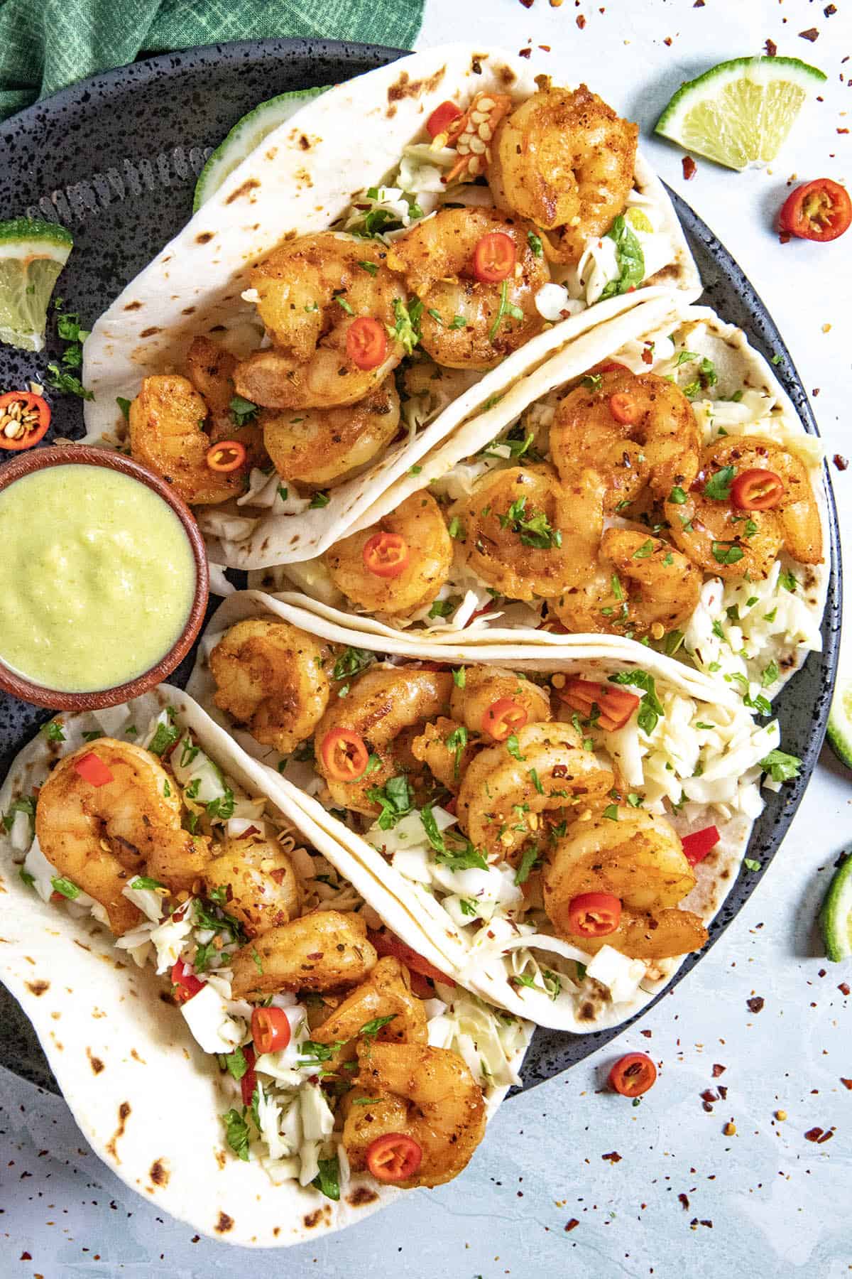 Four fish tacos on a plate served with creamy jalapeno sauce, topped with crunchy slaw