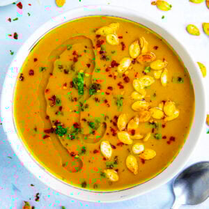 A bowl filled with spicy and creamy pumpkin soup, topped with roasted pumpkin seeds, chili flakes, and a drizzle of oil