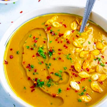 A bowl filled with spicy, silky, creamy pumpkin soup, topped with roasted pumpkin seeds and chili flakes