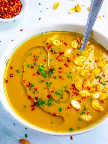 A bowl filled with spicy, silky, creamy pumpkin soup, topped with roasted pumpkin seeds and chili flakes