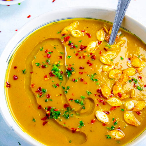 A bowl filled with spicy, silky, creamy pumpkin soup, topped with roasted pumpkin seeds and chili flakes